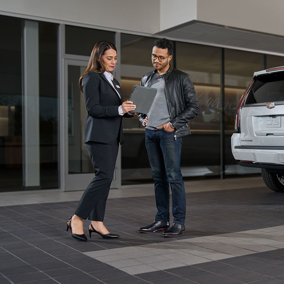 Une personne parle à une guide Cadillac devant un bâtiment moderne.