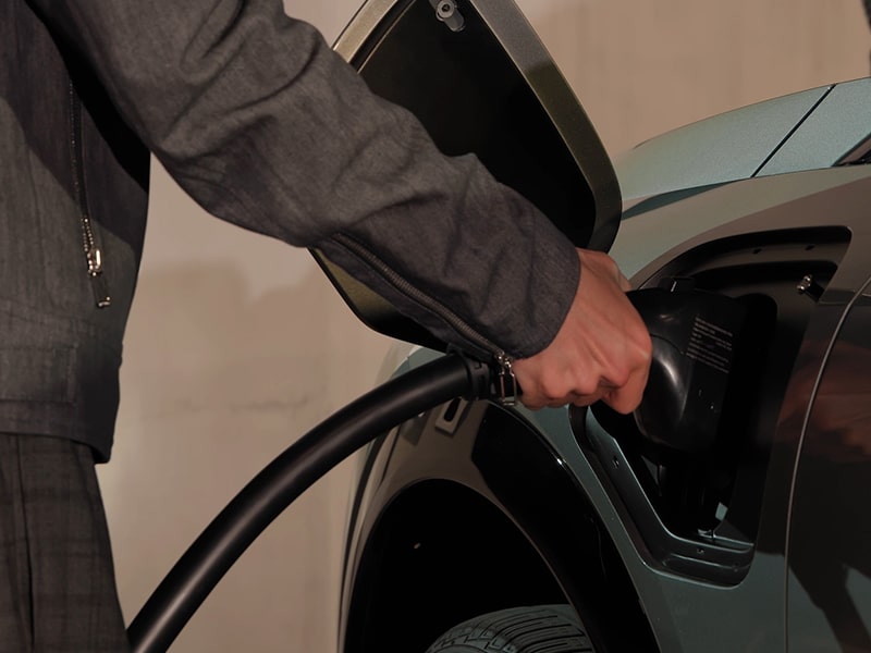 A person charging the 2025 Cadillac OPTIQ electric SUV at a public charging station.