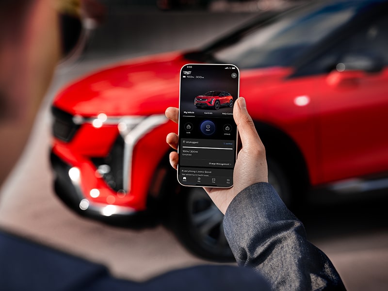 A person looking at his phone near the 2025 Cadillac OPTIQ electric SUV.