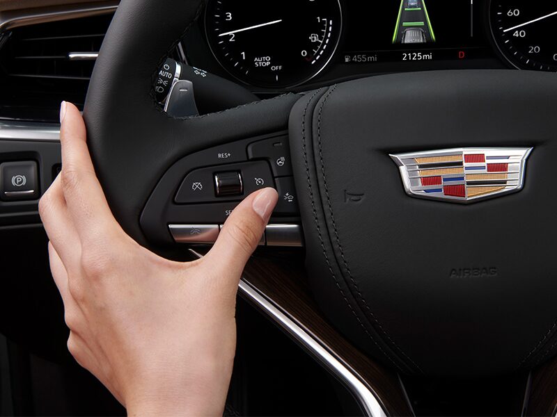 A person pressing buttons on the steering wheel of the 2025 Cadillac XT4.