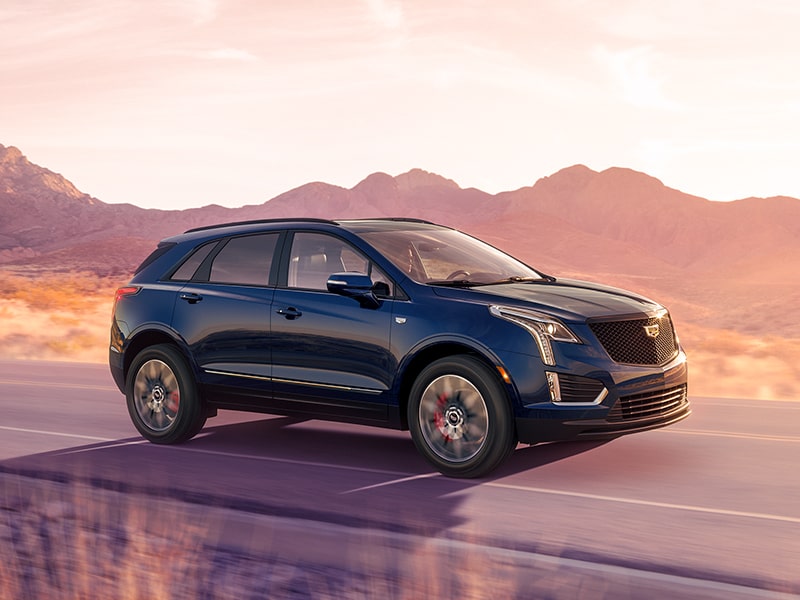 Front-side view of the 2025 Cadillac XT5 luxury SUV driving on a hillside road.