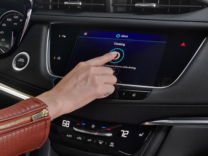 A person pressing the Alexa feature on the infotainment screen of the 2025 Cadillac XT5 luxury SUV.