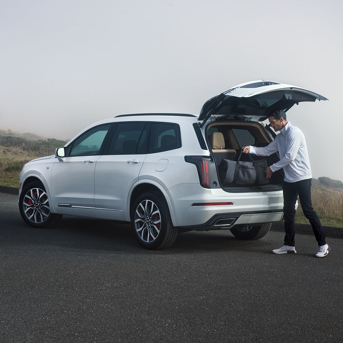 A person stowing his duffel bag on the trunk of the 2025 Cadillac XT6 mid-size 7 passenger SUV.