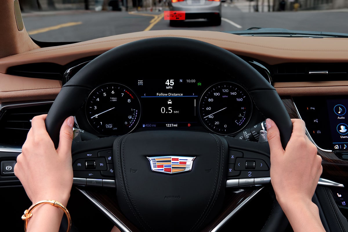 A person holding the steering wheel of the 2025 Cadillac XT6 mid-size 7 passenger SUV .