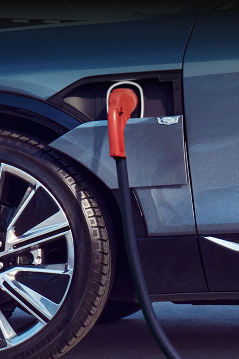 A close-up of a Cadillac electric vehicle, plugged-in and charging.