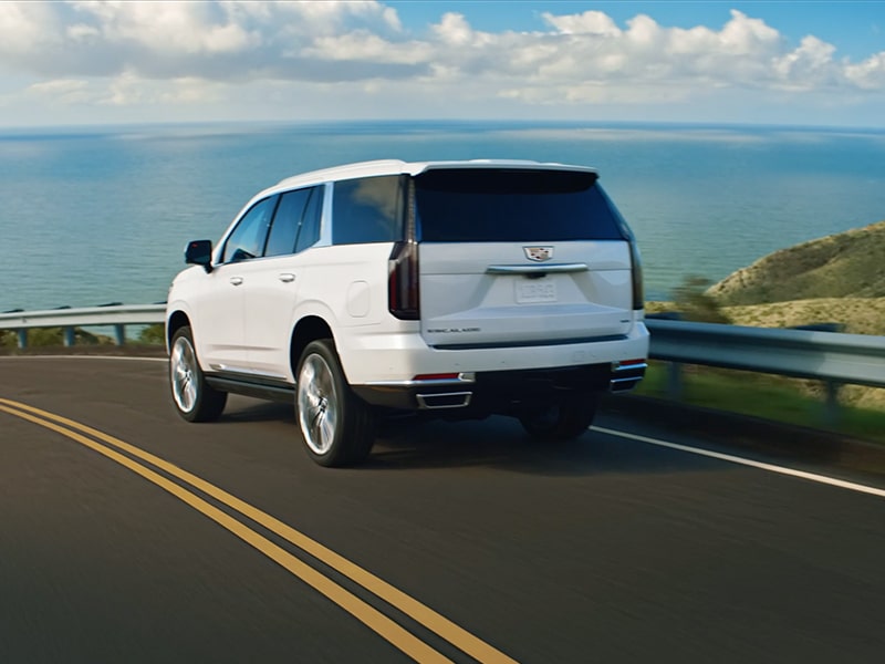 Back view of the 2025 Cadillac Escalade driving near a beachside road.