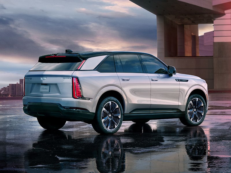 Rear-side view of the 2025 Cadillac Escalade IQ electric suv parked outside a modern home during a cloudy day.