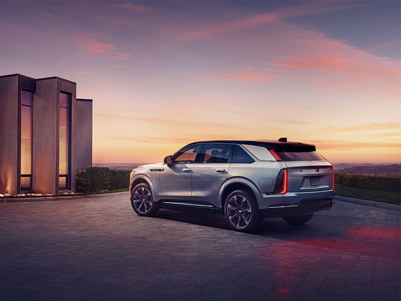 2025 Cadillac Escalade IQ electric suv parked outside a brightly-lit modern home.