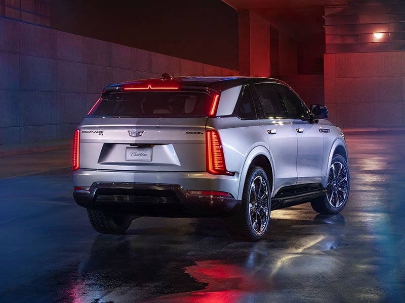 Rear-side view of the 2025 Cadillac Escalade IQ electric suv parked in a brightly lit area. 