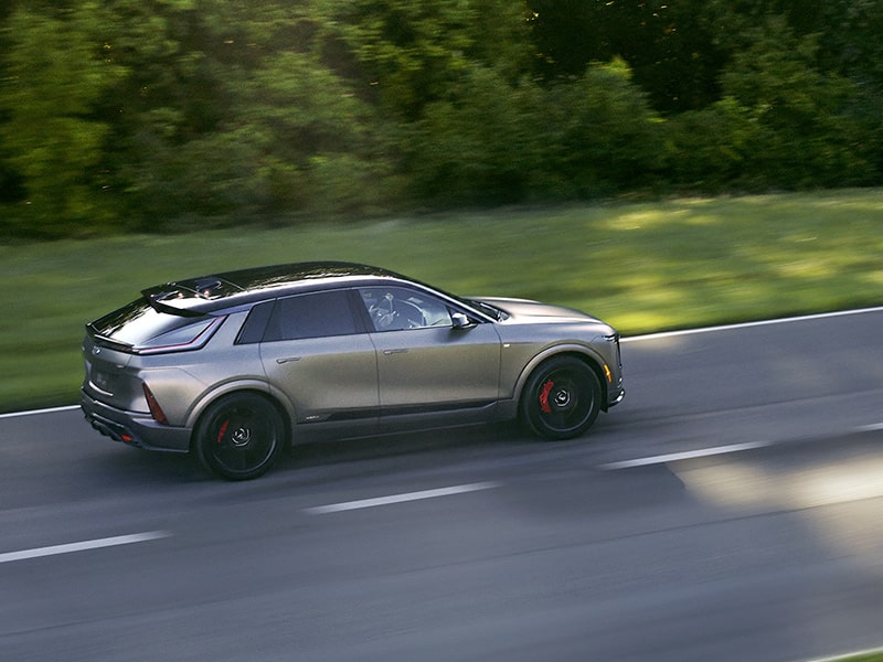 Vue latérale du Cadillac LYRIQ-V 2026 en mouvement seul par une journée ensoleillée.