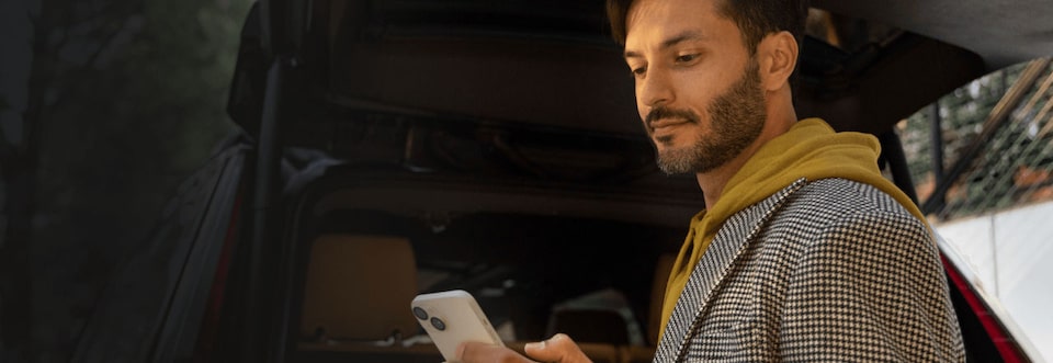 A person looking at his smartphone behind a GM vehicle eligible for GM's Welcome to Canada Program.